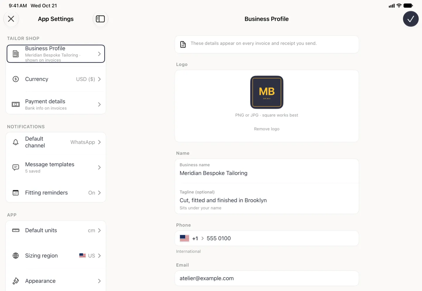 App Settings split view with Business Profile outlined in the settings list on the left, and on the right the Business Profile page with a navy checkmark button at the top right: a note that these details appear on every invoice and receipt you send, a Logo card with the square navy and gold MB logo above PNG or JPG, square works best and a Remove logo link, a Name card with Business name Meridian Bespoke Tailoring and Tagline (optional) Cut, fitted and finished in Brooklyn, noted Sits under your name, then the Phone field with a US flag, +1 and 555 0100, and the shop email address in the Email field.
