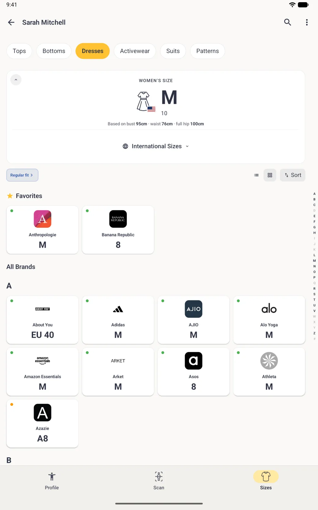 A Sizes tab for Dresses sorted A to Z in the grid view, with the folded size card (M, 10, US flag) and the toolbar at the top, a Favorites row with Anthropologie M and Banana Republic 8, then a four-column grid under the heading A: About You EU 40, Adidas M, AJIO M, Alo Yoga M, Amazon Essentials M, Arket M, Asos 8, Athleta M and Azazie A8 (orange dot), the B heading at the bottom edge, and a thin alphabet index down the right edge.