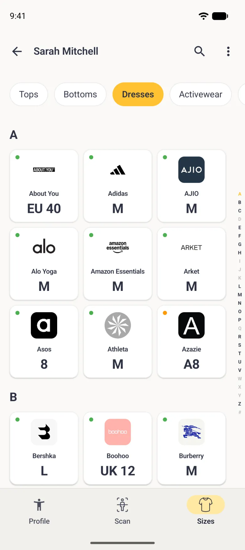 A Sizes tab for Dresses sorted A to Z in the grid view, scrolled to the letter A with the size card above it out of view, showing a three-column grid of brand logo cards under the heading A: About You EU 40, Adidas M, AJIO M, Alo Yoga M, Amazon Essentials M, Arket M, Asos 8, Athleta M and Azazie A8 (orange dot), then the B group with Bershka L, Boohoo UK 12 and Burberry M, each with a green dot, and a thin alphabet index down the right edge with A in gold.