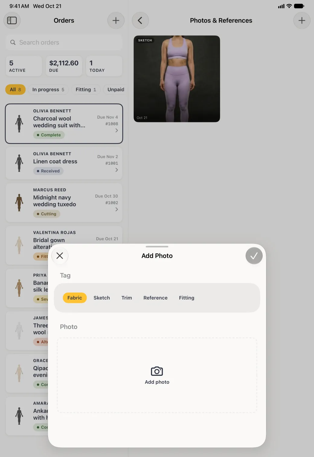 Add Photo sheet rising from the bottom over the dimmed Orders list and the Photos and References pane, which already shows one Sketch photo, with a grab handle, a close button at the top left and a dimmed round tick at the top right, tag chips reading Fabric, Sketch, Trim, Reference and Fitting with Fabric selected in gold, and an empty dashed Add photo area with a camera icon.